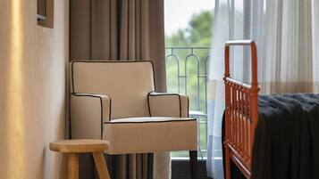 A room with a sofa, a small stool, a bed, and a balcony with curtains.