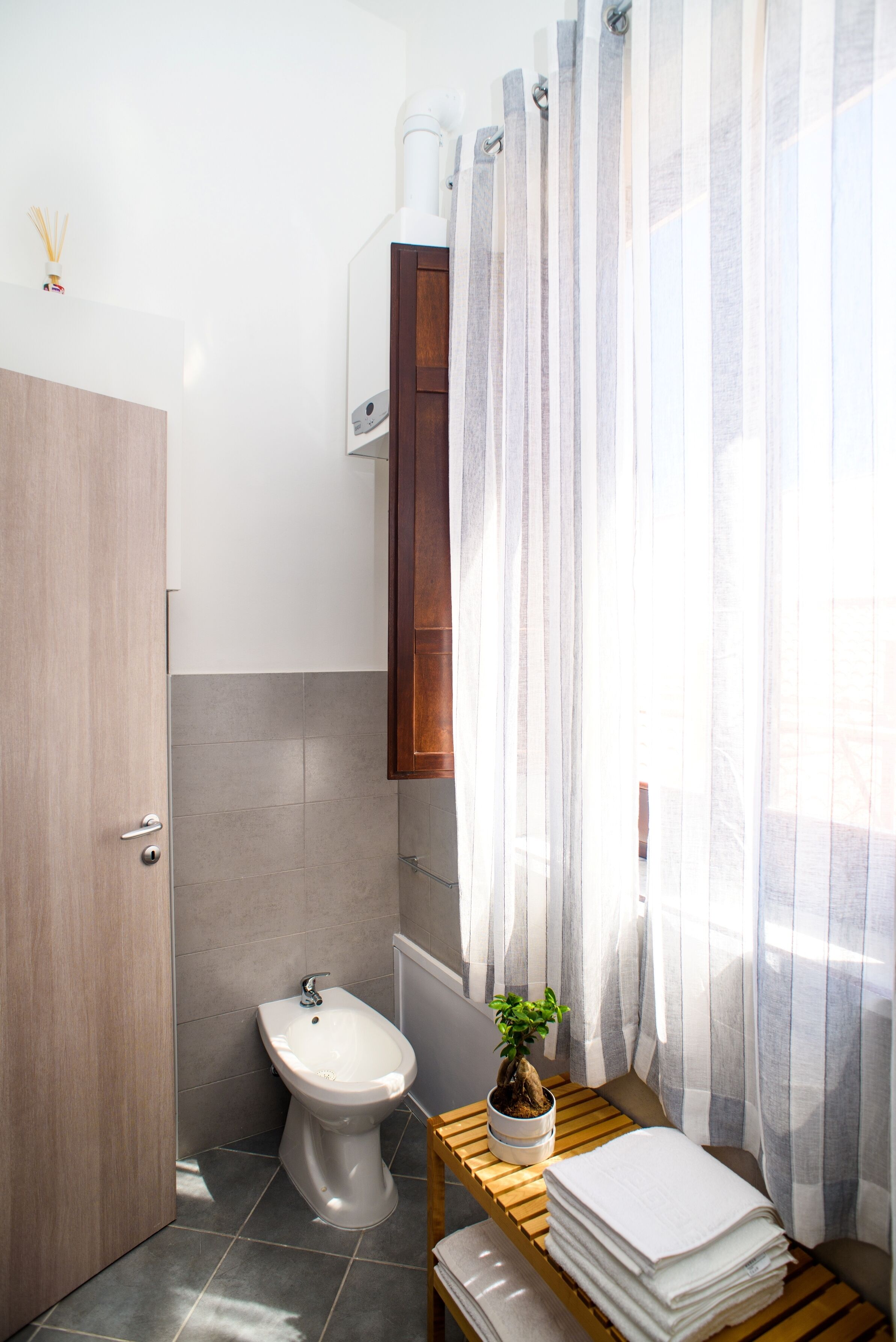 Un baño con bidé, un mueble de madera, una mesita con una planta y una pila de toallas.