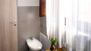 Un baño con bidé, un mueble de madera, una mesita con una planta y una pila de toallas.