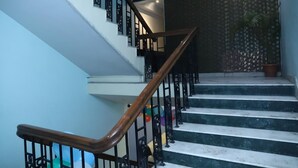 A staircase with wooden handrails and black metal railings, leading to a landing with a patterned wall and a potted plant. - Airport Hotel Golden Jindal (New Delhi)