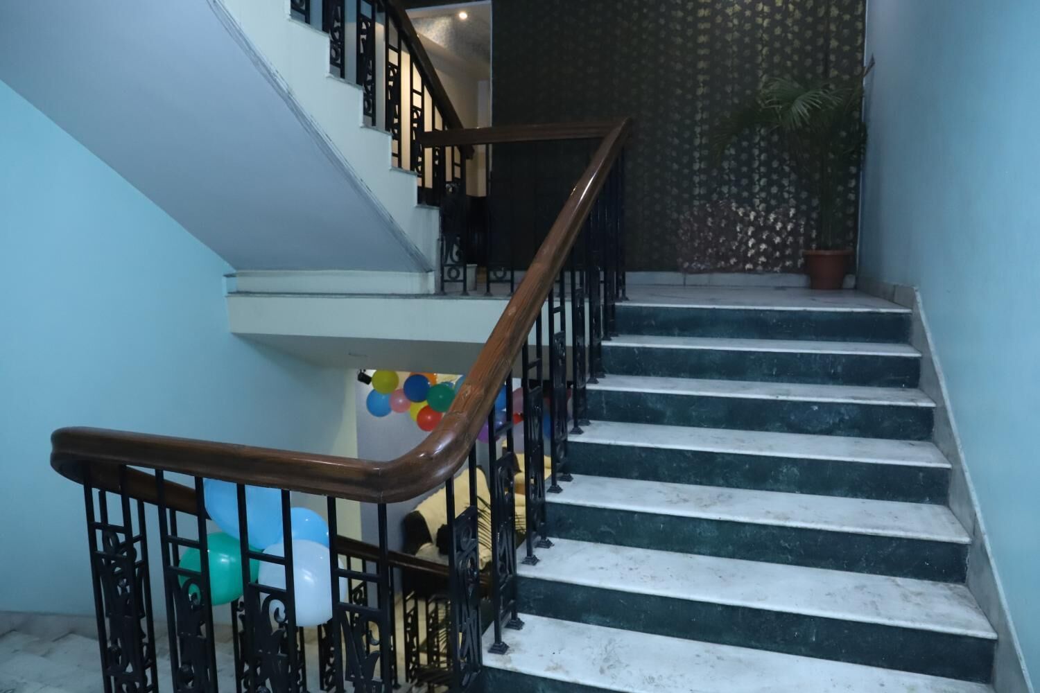 Un escalier avec une main courante en bois et des rampes en métal noir, menant à un palier décoré de ballons.
