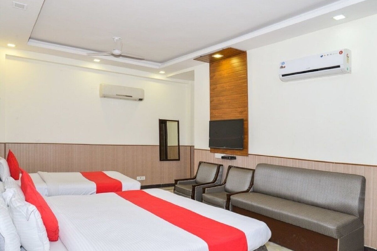 A hotel room with two beds, a sofa, a TV, and an air conditioning unit.