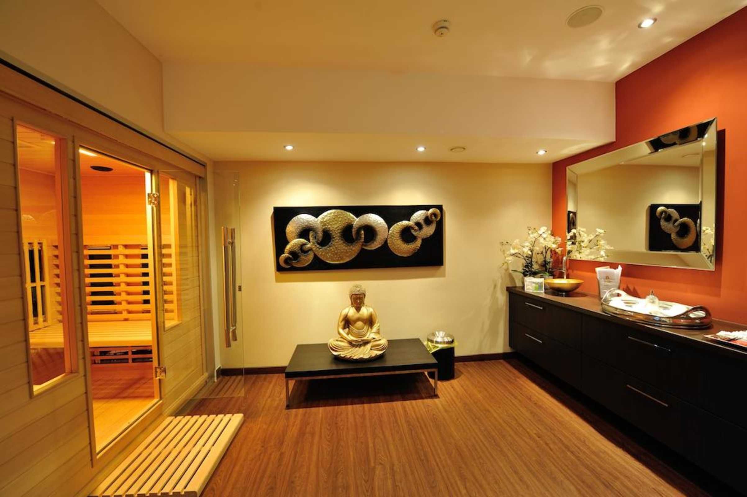 Une salle de bain moderne avec un plancher en bois, un grand miroir, une statue de Bouddha et une œuvre d’art accrochée au mur.