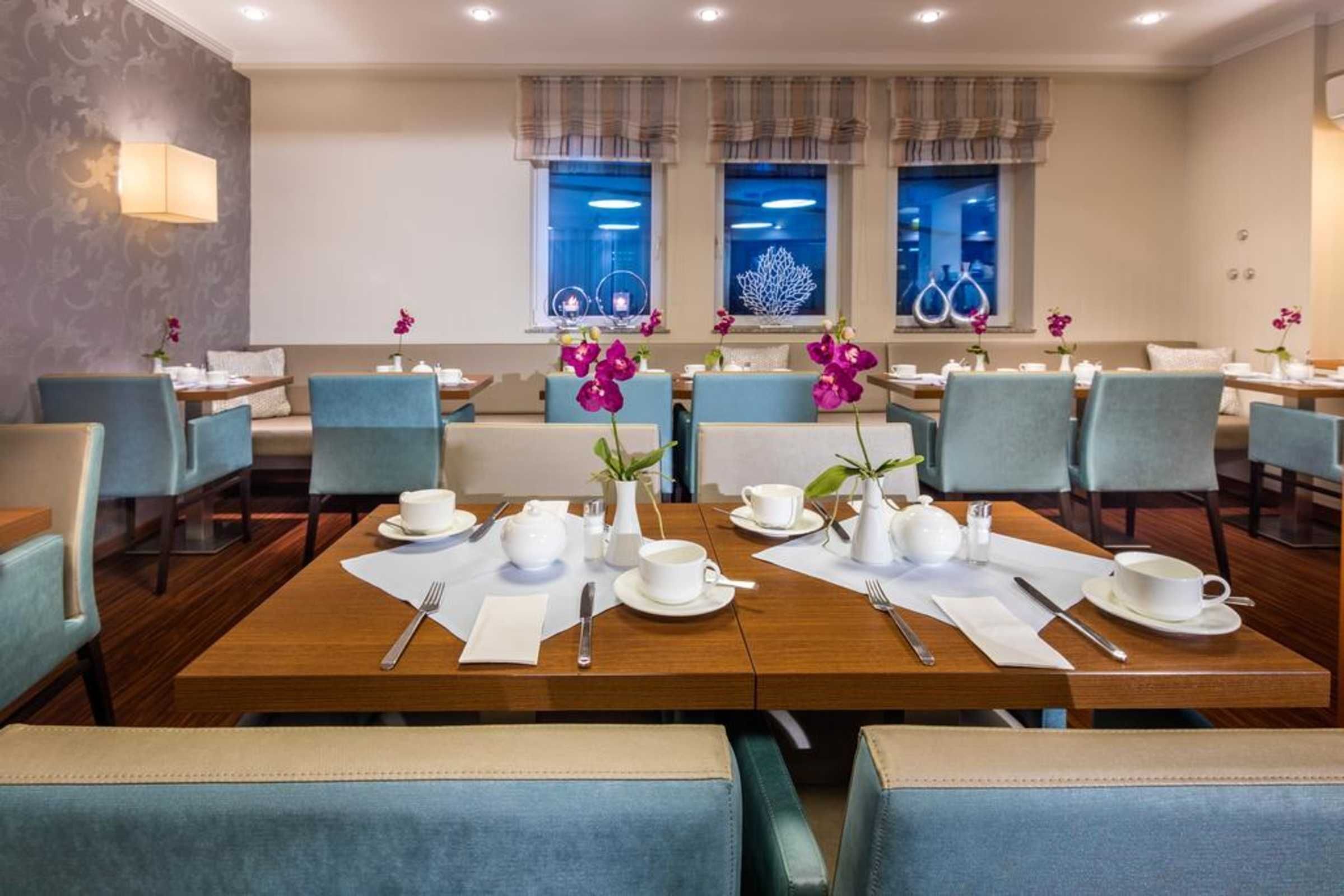 Une salle à manger d’hôtel avec de nombreuses tables et chaises, chacune agrémentée de vaisselle blanche et d’orchidées violettes.