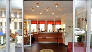 Ein Hotel-Empfangsbereich mit einem Holzbüro, roten Vorhängen und einem modernen Deckenstil.