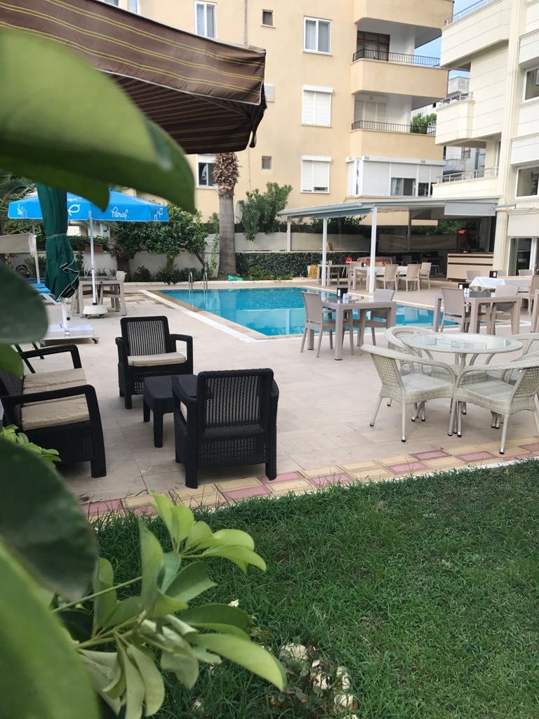 An outdoor pool area with lounge chairs and tables, surrounded by a building with balconies.
