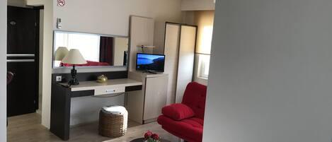 Un espacio habitable compacto con kitchenette, comedor y zona de estar con una silla roja.