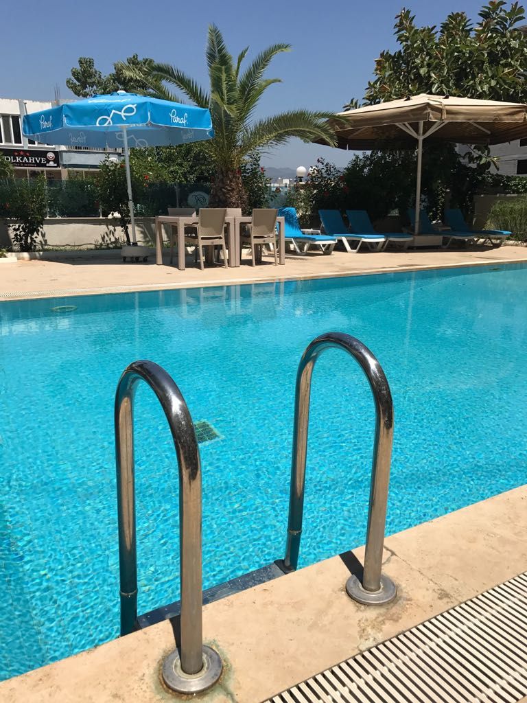 Ein Schwimmbecken mit Metallhandläufen, Liegestühlen und Sonnenschirmen.