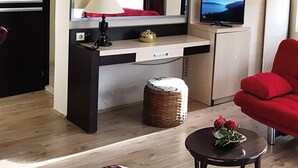 Un espacio habitable compacto con kitchenette, televisor de pantalla plana, un sillón rojo y una pequeña mesa con un florero.