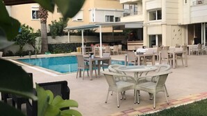 Zona junto a la piscina con mobiliario exterior y vistas a un edificio de varios pisos.
