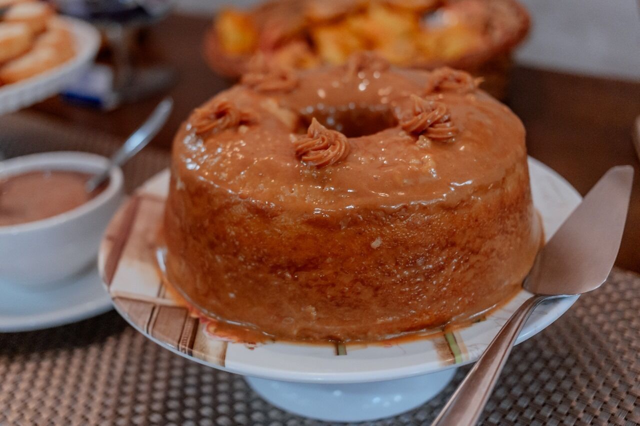 A round cake with a glossy glaze and decorative swirls on top, placed on a white plate with a spoon beside it.