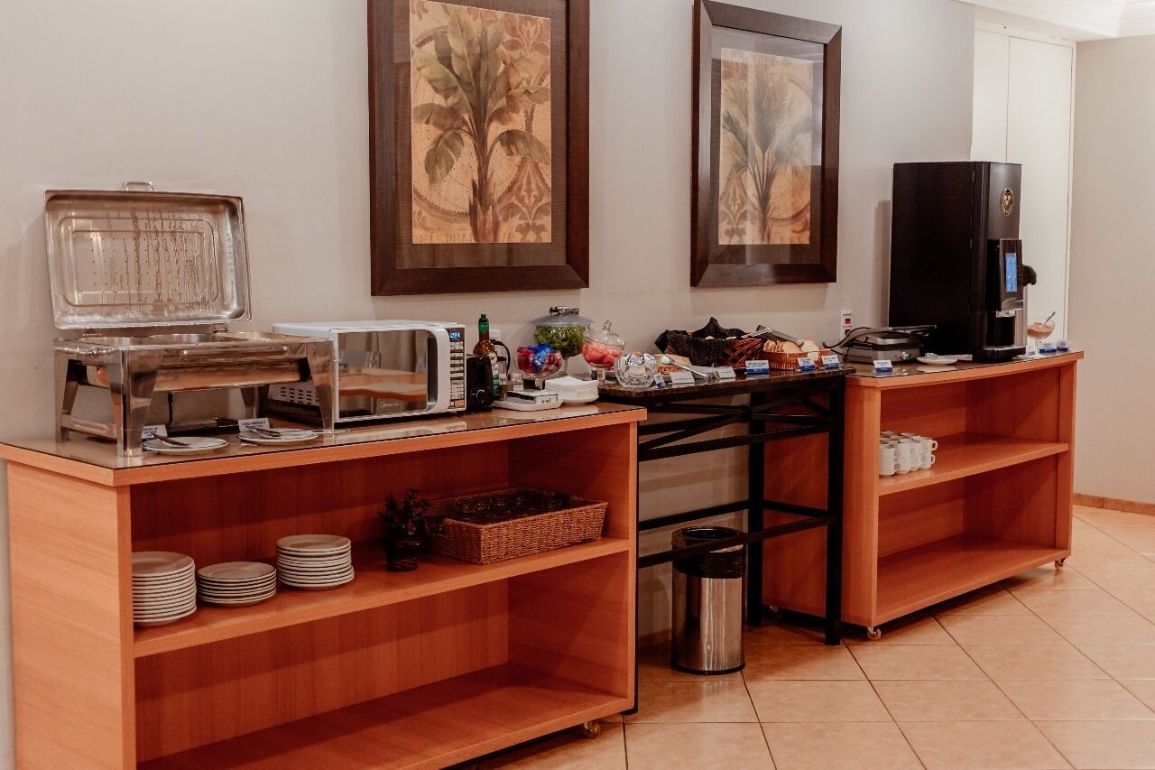 A buffet setup with a coffee machine, microwave, and various food items on a wooden counter.