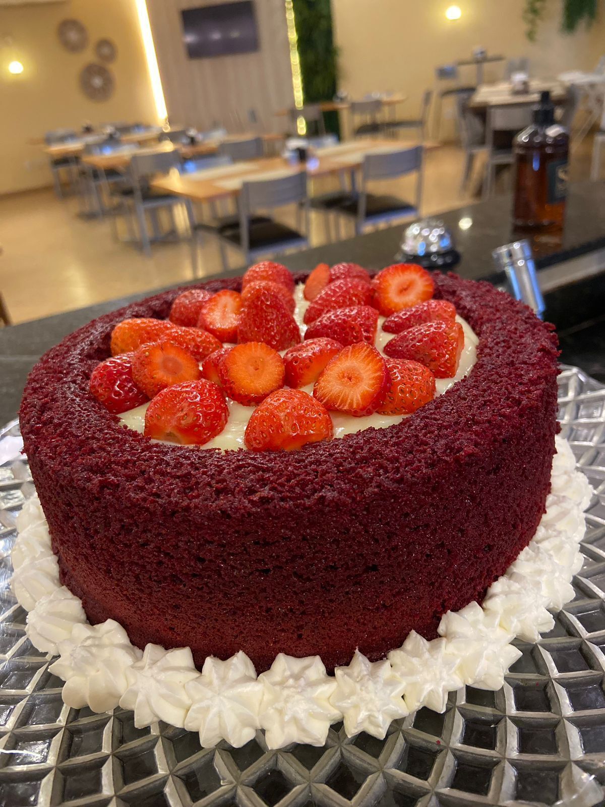Un pastel redondo de terciopelo rojo con fresas y crema sobre un plato de vidrio.