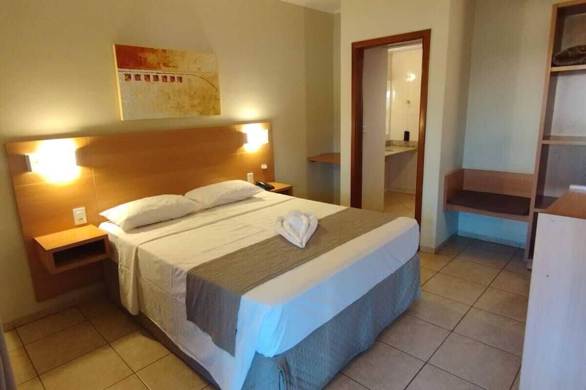 Une chambre d’hôtel avec un lit, des tables de chevet, une armoire et une salle de bain visible à travers une porte ouverte.