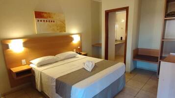 Una habitación de hotel con una cama, mesitas de noche, un armario y un baño visible a través de una puerta abierta.