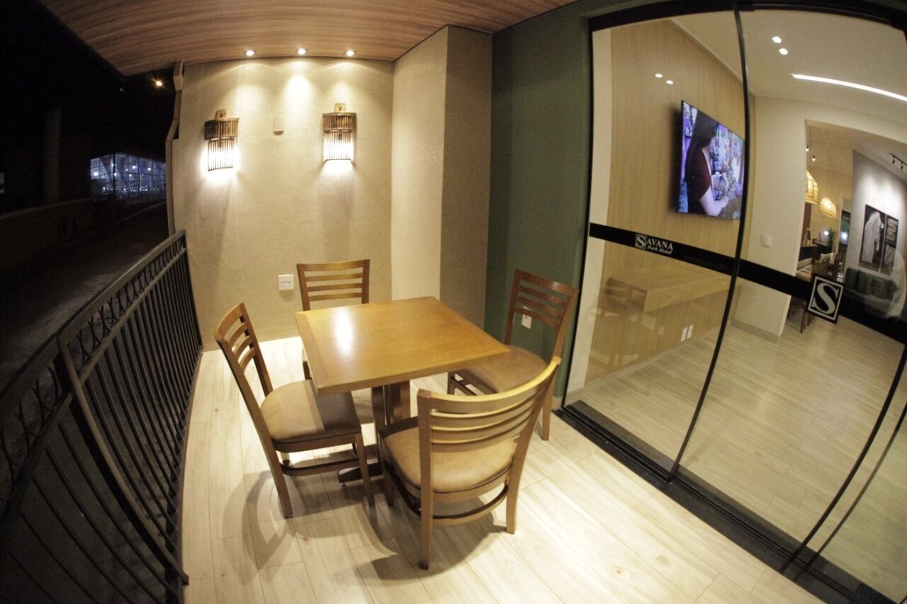 Un espace repas avec une table et des chaises en bois, une cloison en verre avec un téléviseur, et un escalier menant à un niveau supérieur.