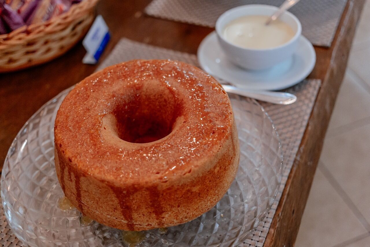 A bundt cake on a glass plate with a bowl of cream on a table.