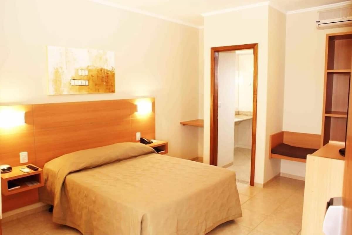 Une chambre d’hôtel avec un lit, une table de chevet, une lampe et une tête de lit en bois.