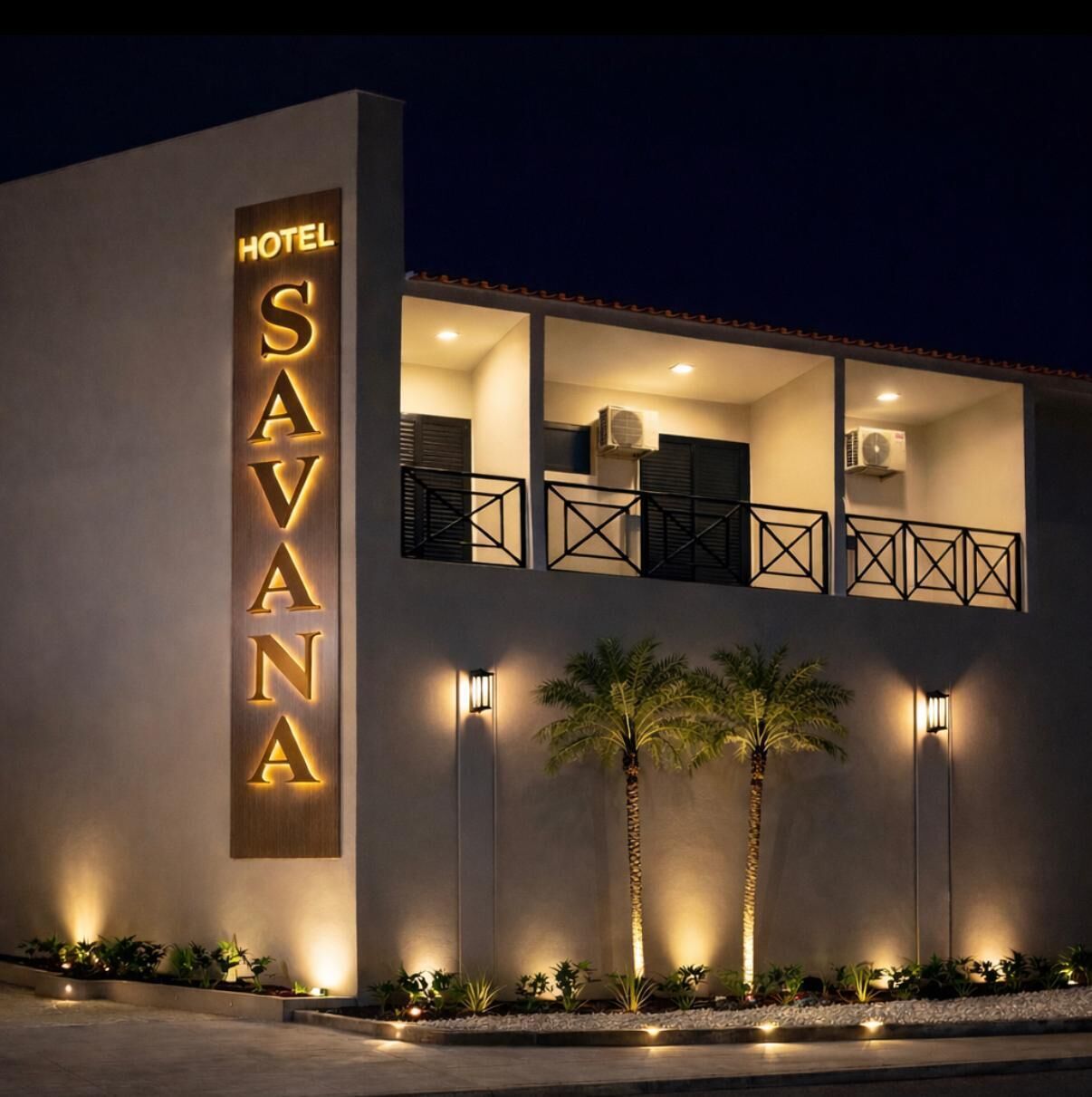 Un hôtel moderne, reconnaissable à son grand panneau « SAVANA », doté d’un balcon avec une balustrade et de deux palmiers en premier plan.