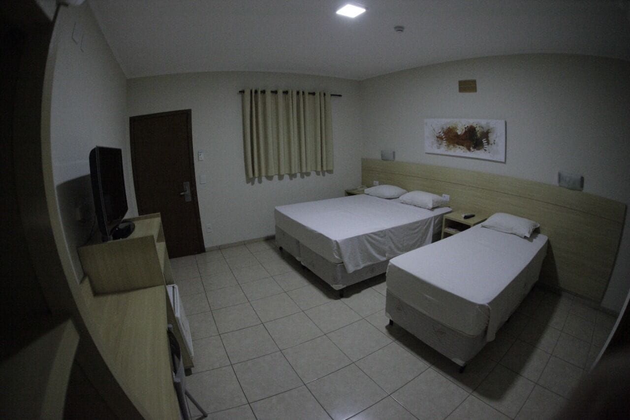Une chambre d’hôtel avec deux lits simples, une tête de lit en bois, un téléviseur à écran plat, une porte et un rideau.