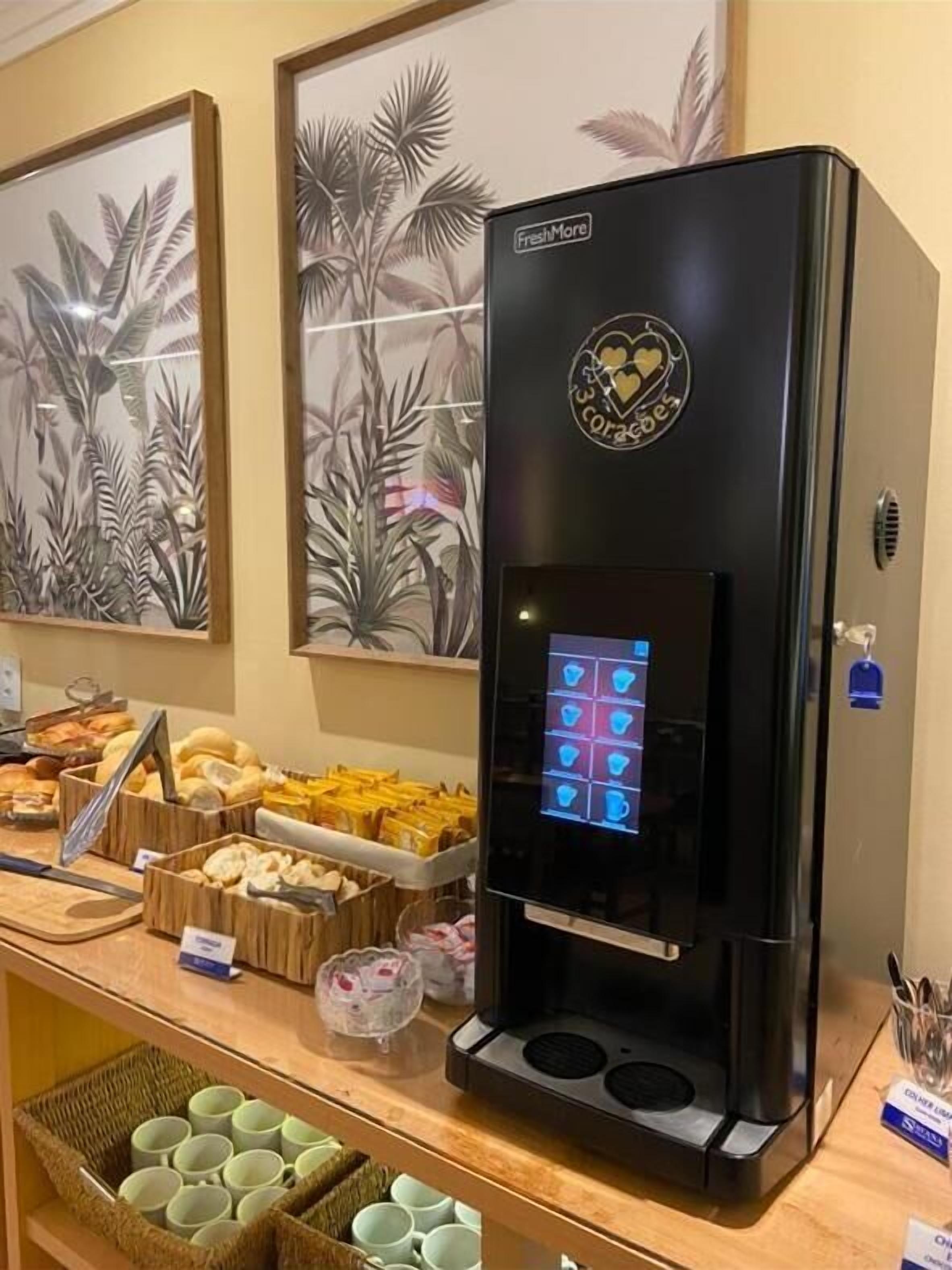 Una cafetera con pantalla digital, rodeada de alimentos y cestas de tazas.