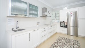 Une cuisine moderne avec des meubles blancs, un réfrigérateur en acier inoxydable, un four encastré et une fenêtre au-dessus de l’évier.