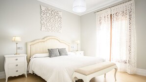 Une chambre à coucher comprenant un lit, deux tables de chevet, un banc, un élément décoratif mural et une fenêtre avec des rideaux.