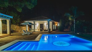 Une vue nocturne d’une maison avec une piscine, un espace salon extérieur et un mur en pierre.