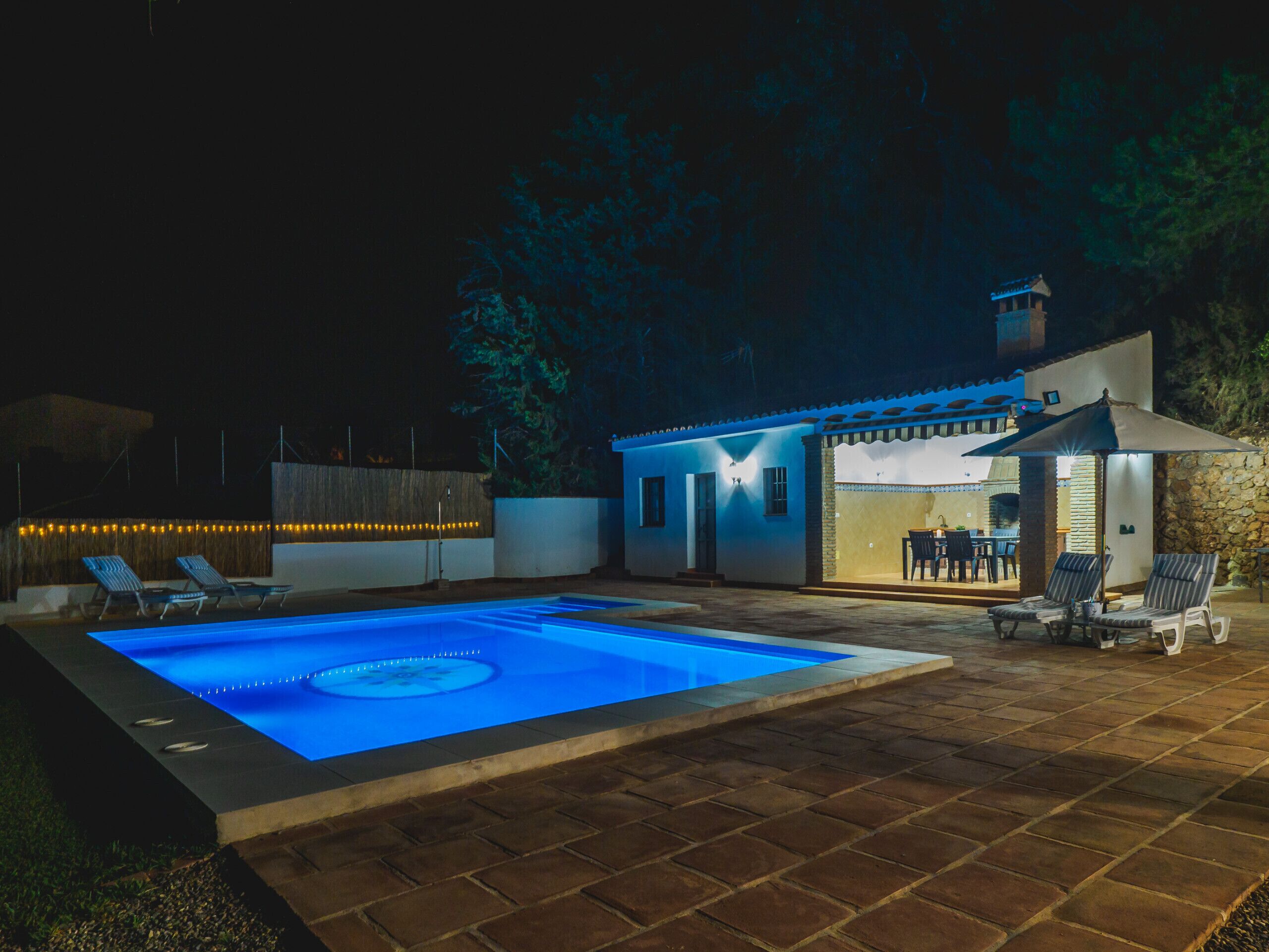 A nighttime swimming pool area with a patio and lounge chairs.