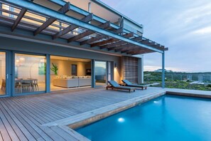 Una casa moderna con piscina, comedor y cocina visibles a través de puertas de vidrio.