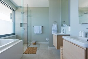 A modern bathroom with a glass shower enclosure, a large bathtub, and a wooden vanity with a sink. - Roman's Villa (Gansbaai)