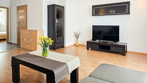 A modern living room with a wooden floor, a black entertainment unit, a flat-screen TV, a bench, and a vase with yellow flowers. - 2-room WO07 - Platan (WO07) (Swinoujscie)