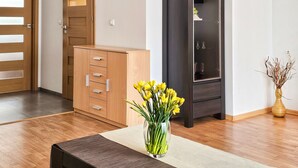 A room with a wooden door, a cabinet with drawers, a tall dark cabinet, a vase with yellow flowers, and a woven mat on the floor. - 2-room WO07 - Platan (WO07) (Swinoujscie)