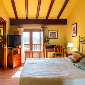 A bedroom with a bed, a desk, a chair, a television, and a window with a view.