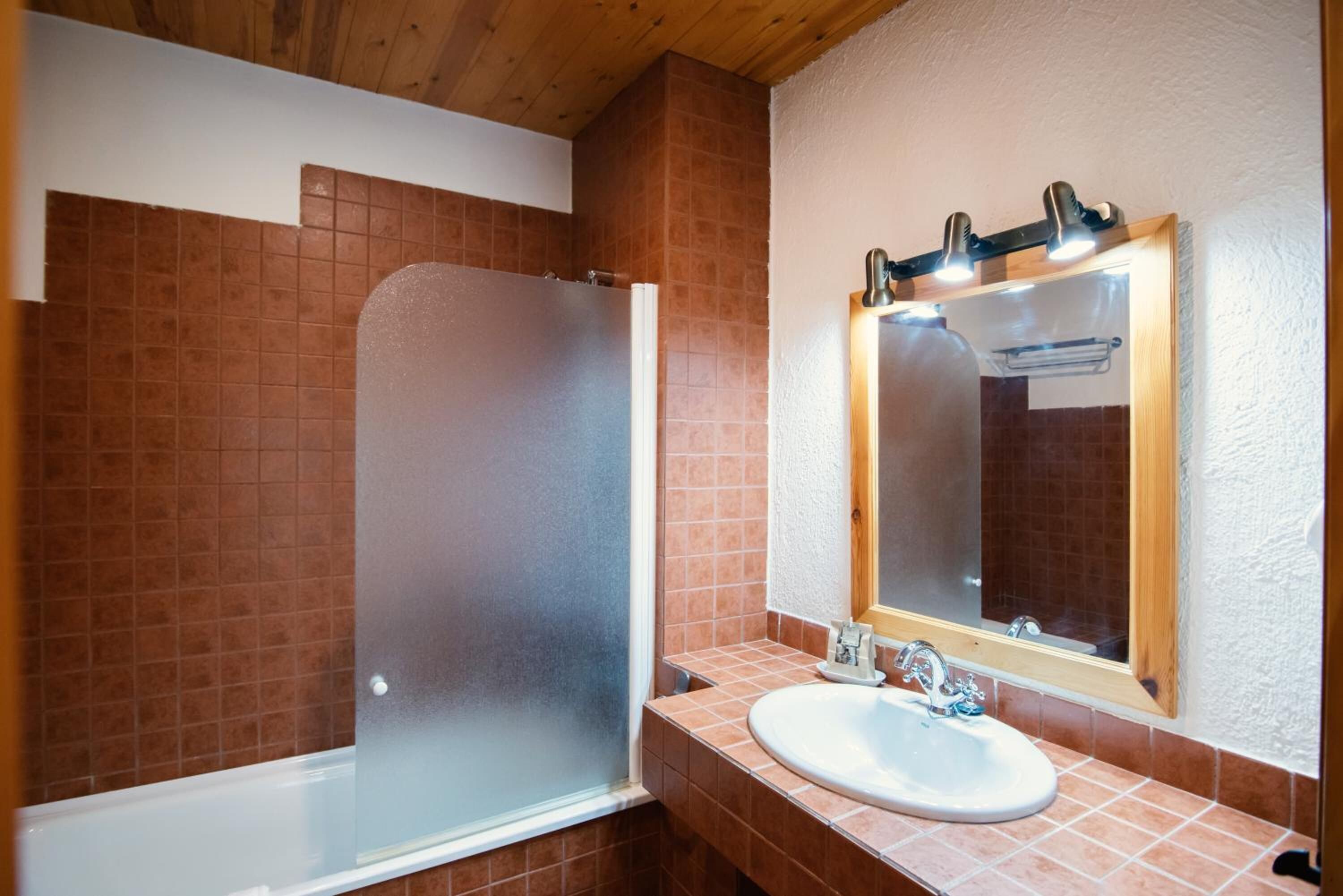 Un baño con cabina de ducha de vidrio, un lavamanos blanco y un espejo con luces arriba.
