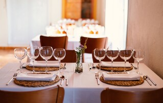 Una mesa de comedor dispuesta con varias copas de vino, un florero con flores y un mantel tejido.