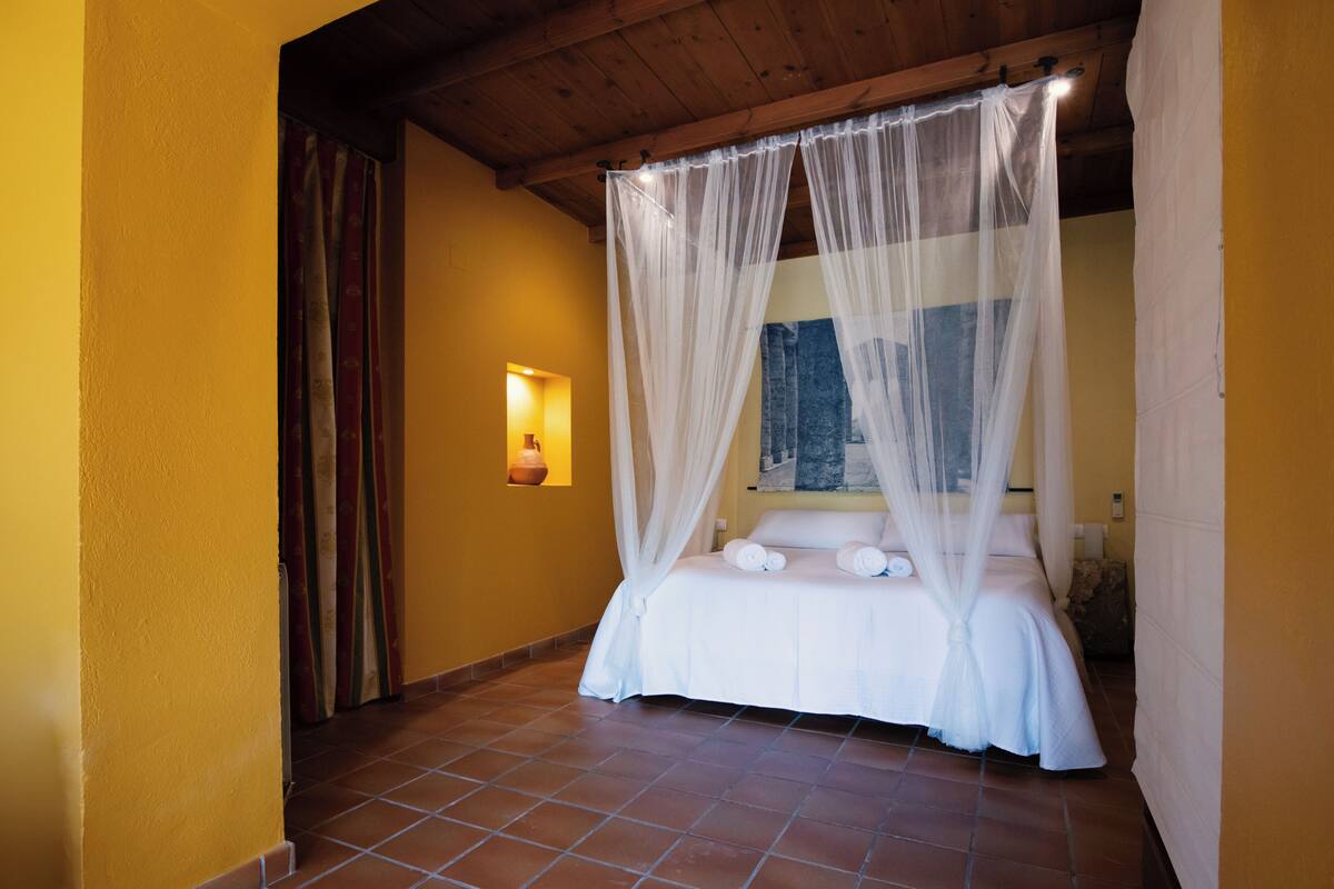 Un dormitorio con cama con dosel, una lámpara de pared y suelo de baldosas.