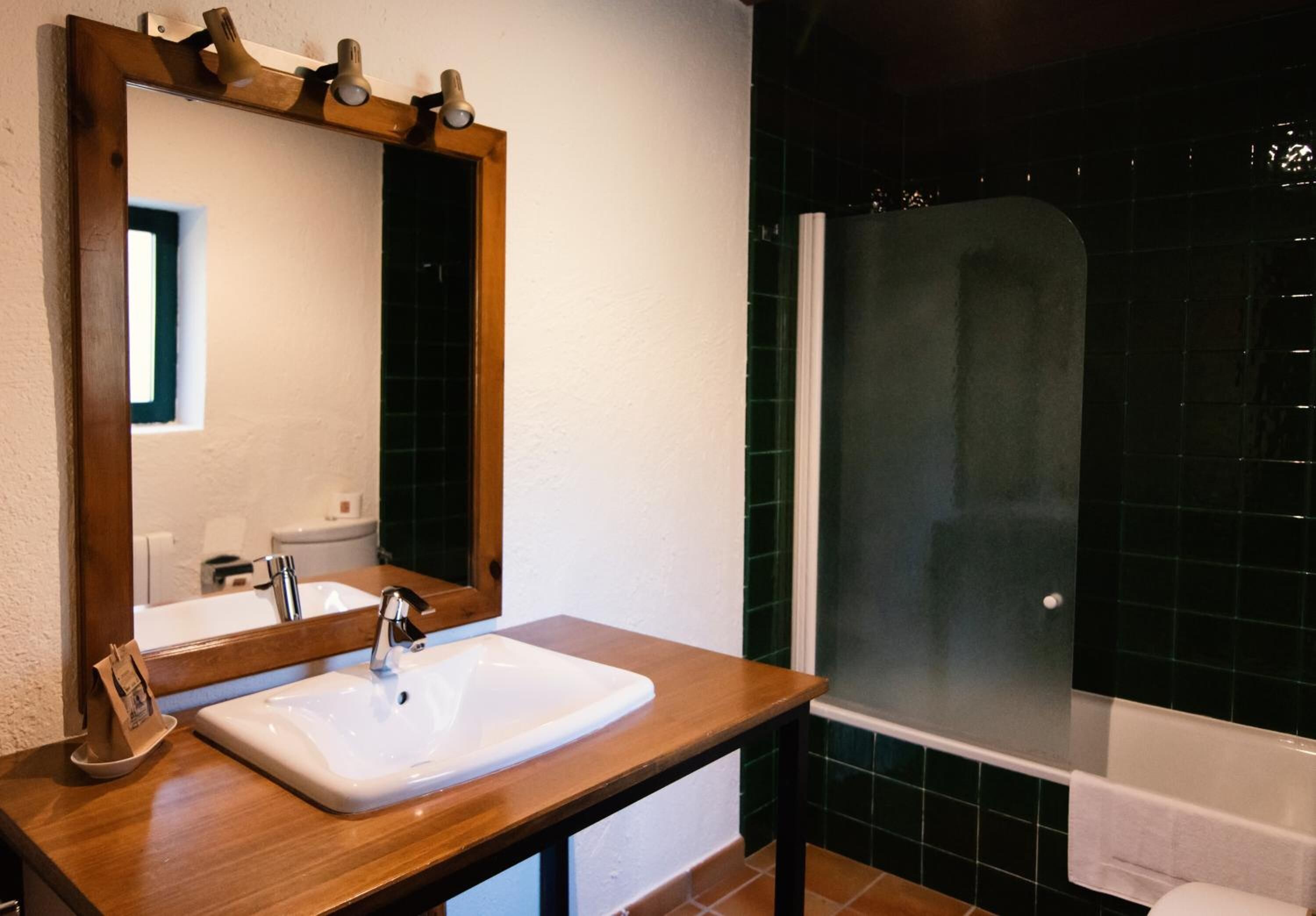 A bathroom with a wooden vanity, a white sink, a mirror, and a glass-enclosed shower.