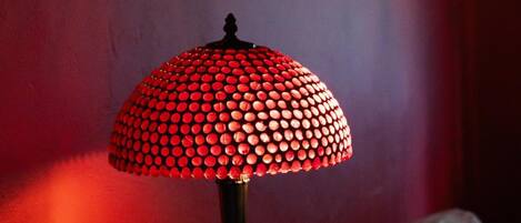 Una lámpara de mesa con una pantalla roja a lunares sobre una mesa de madera, con dos lámparas fijadas a la pared al fondo.