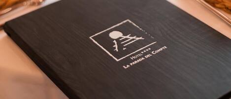 A black menu with the text "Hotel La Parada del Sol" on a table set with white napkins, cutlery, and woven placemats.