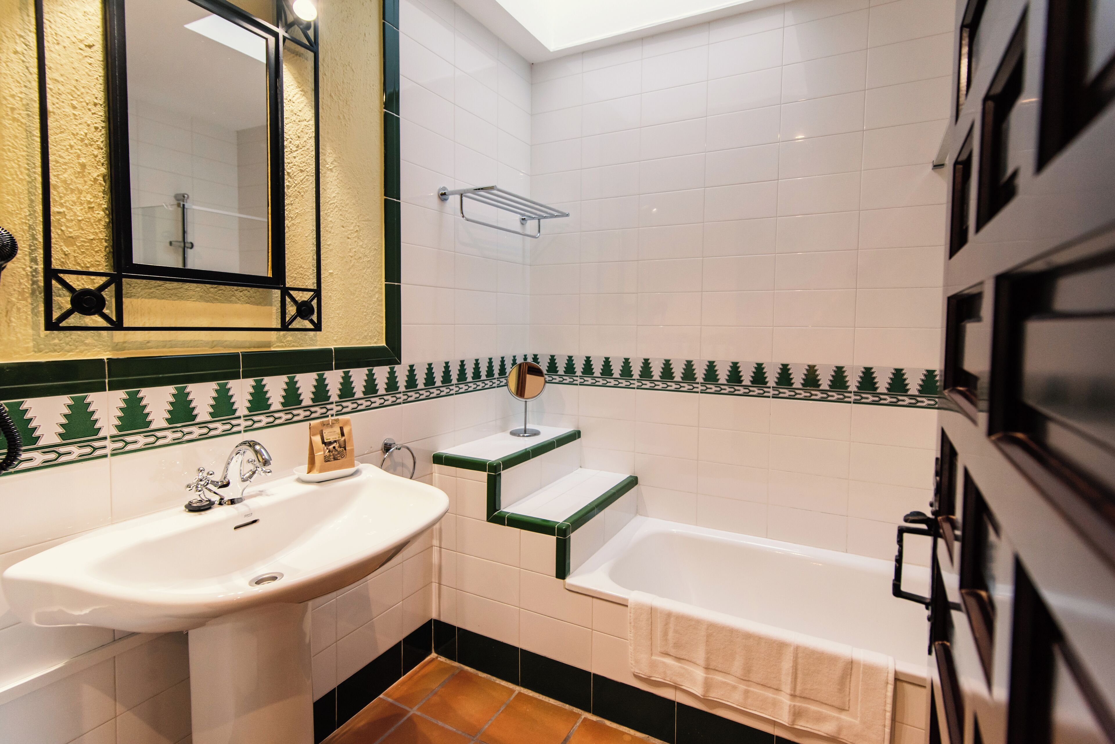 Une salle de bain avec un lavabo blanc, un miroir, une douche carrelée de carreaux verts et une baignoire.