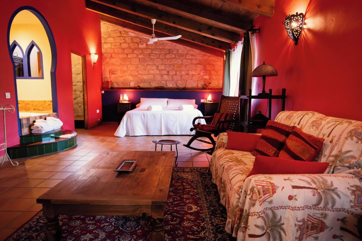 Una habitación acogedora con una cama, un sillón mecedor, una mesita de centro de madera y una alfombra estampada.