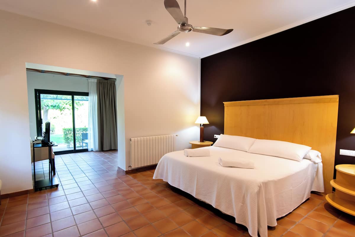 Habitación de hotel con una cama grande, ventilador de techo, escritorio con lámpara y vistas al exterior a través de una puerta corredera.