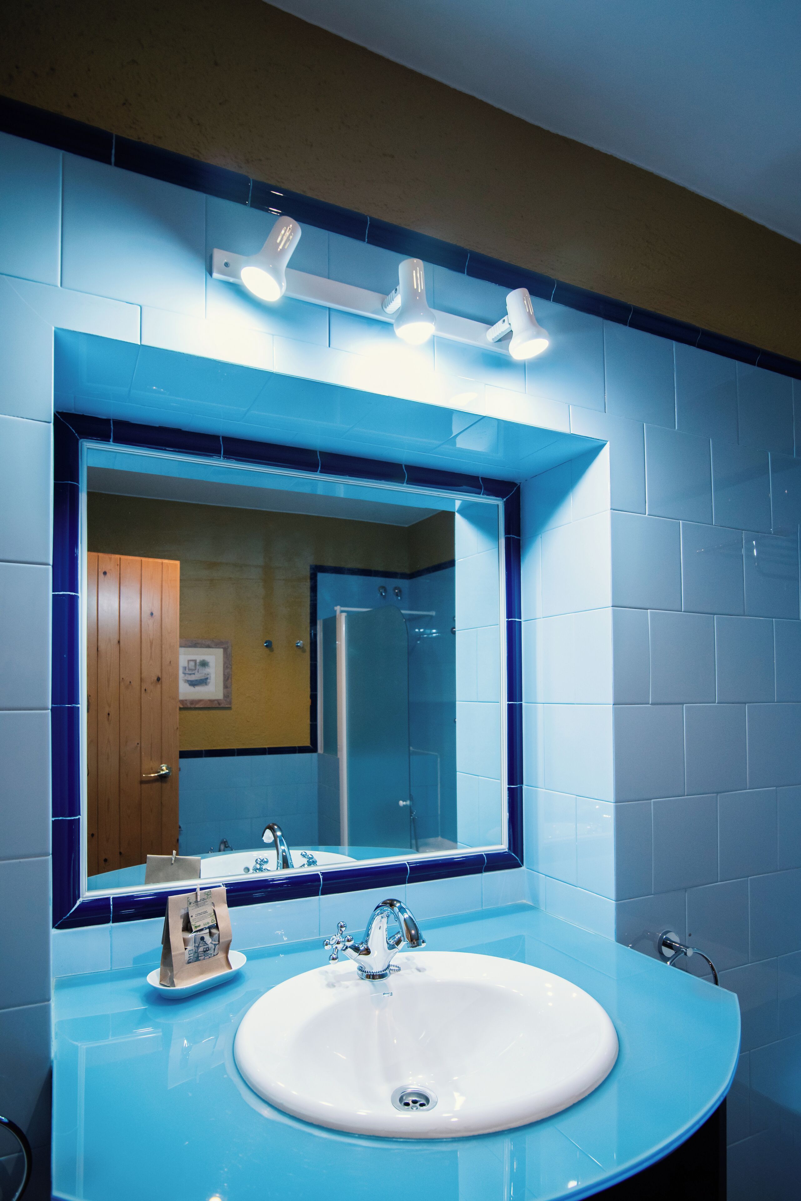 A bathroom with a blue-tiled wall, a white sink, and a mirror above it.