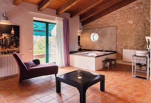 Una habitación moderna con pared de piedra, una mesa de vidrio, un sofá morado y vista a la ciudad.