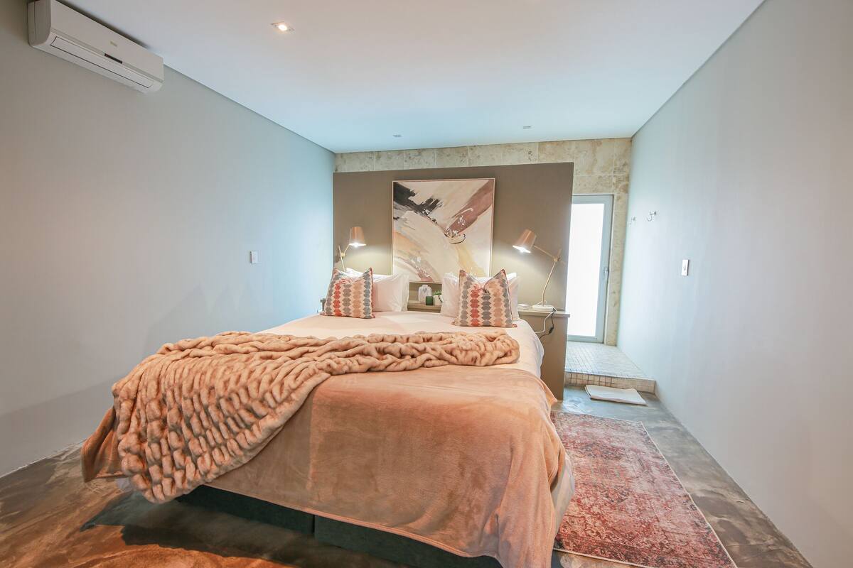 A modern bedroom with a large bed, a red rug, and a painting on the wall.