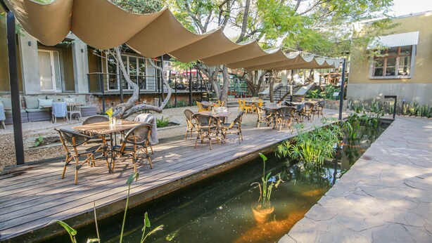 A wooden deck with outdoor seating, a small water feature, and shaded areas with canopies. - Suite 9 The Village (Windhoek)