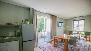 A kitchen with a dining area, a refrigerator, a sink, and a window with curtains. - Suite 9 The Village (Windhoek)