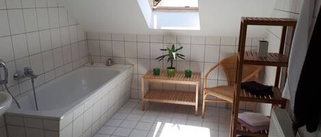 A bathroom with a skylight, a bathtub, a toilet, a chair, a shelf, and a radiator.