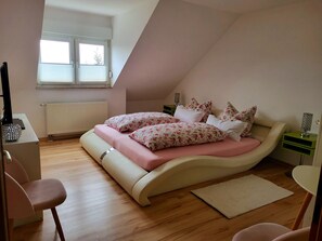 A bedroom with a bed, a chair, a desk, a radiator, and a window.